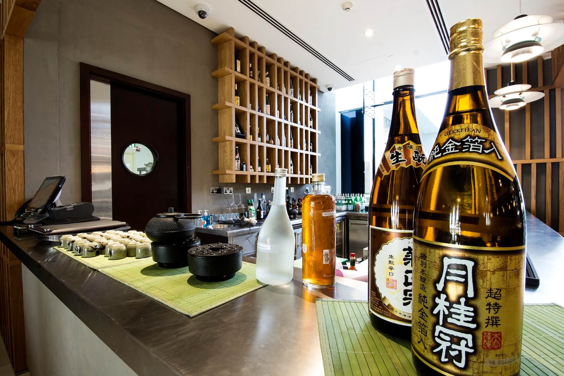 Modern Japanese sake bar with bottles, display shelves, traditional vessels, and dark door entrance.