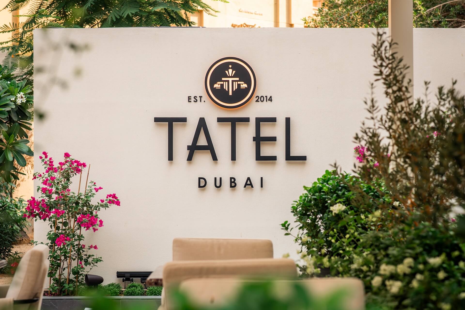 Tatel Dubai restaurant entrance sign with Est. 2014 logo, surrounded by pink flowers and green plants