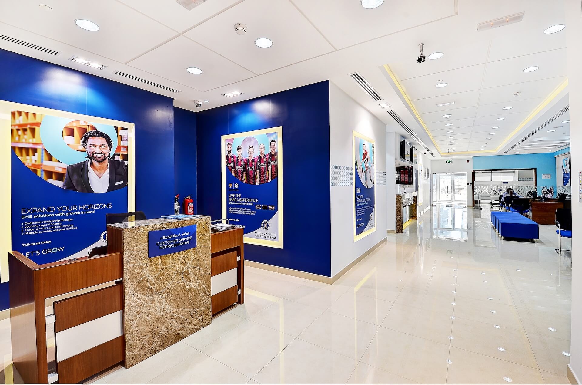 Modern bank branch interior with blue accent walls, reception desk, and promotional displays.