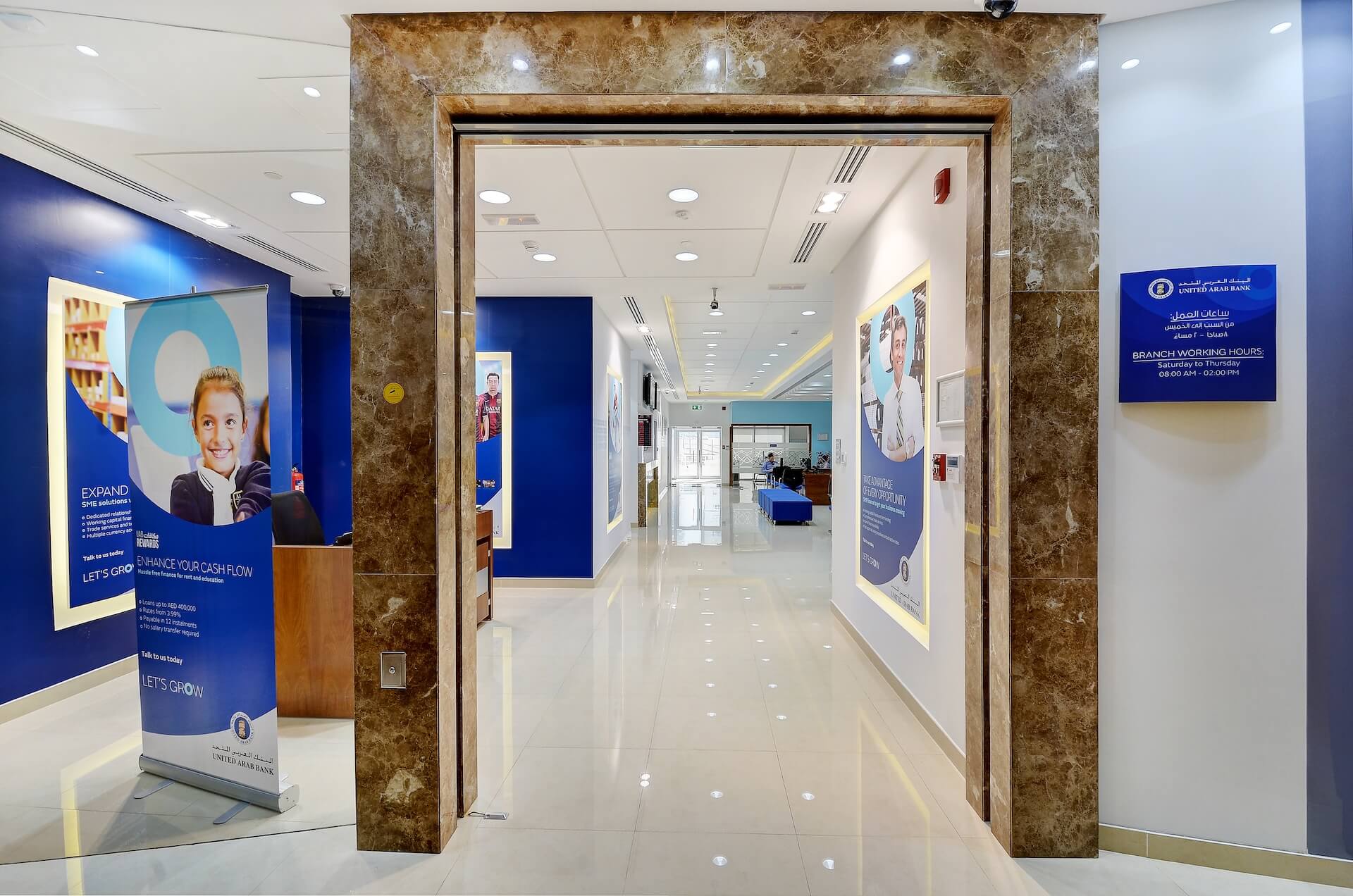 Modern bank branch entrance with marble frame, blue marketing displays, and professional interior design.