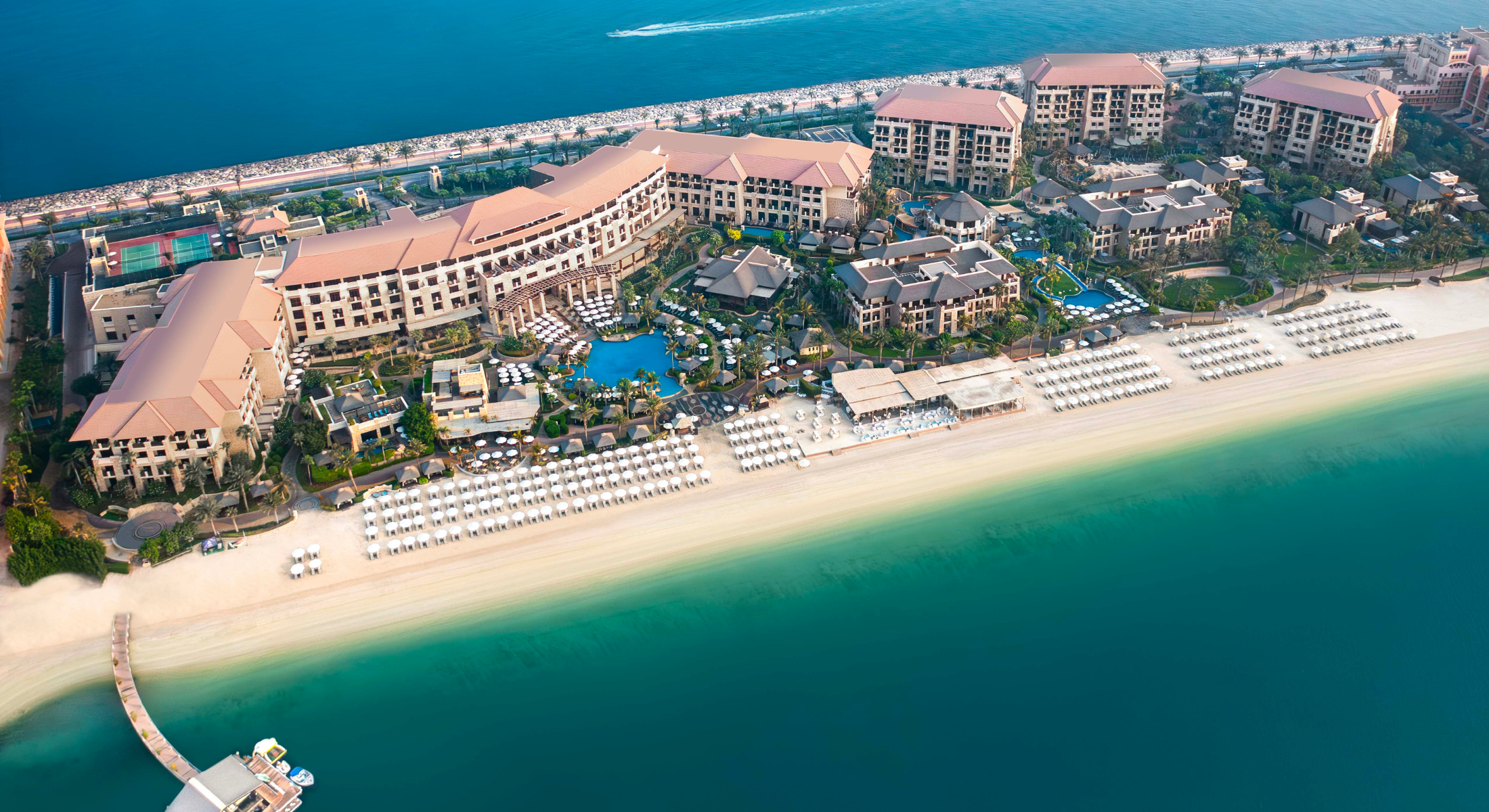 Aerial view of luxury beachfront resort with turquoise ocean, sandy beach, and modern buildings