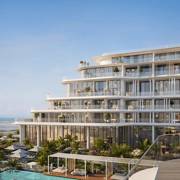 Modern curved beachfront building with multiple balconies, gardens, and pool overlooking ocean.