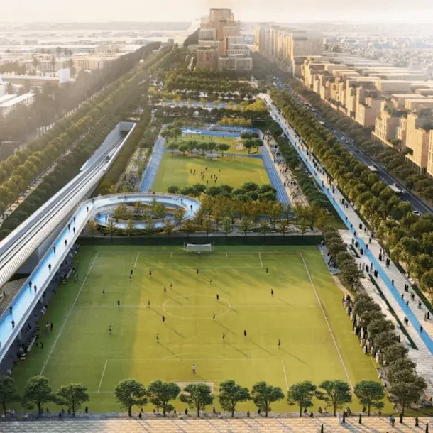 Aerial view of urban sports complex with soccer fields, pools, and recreational areas along tree-lined boulevard.