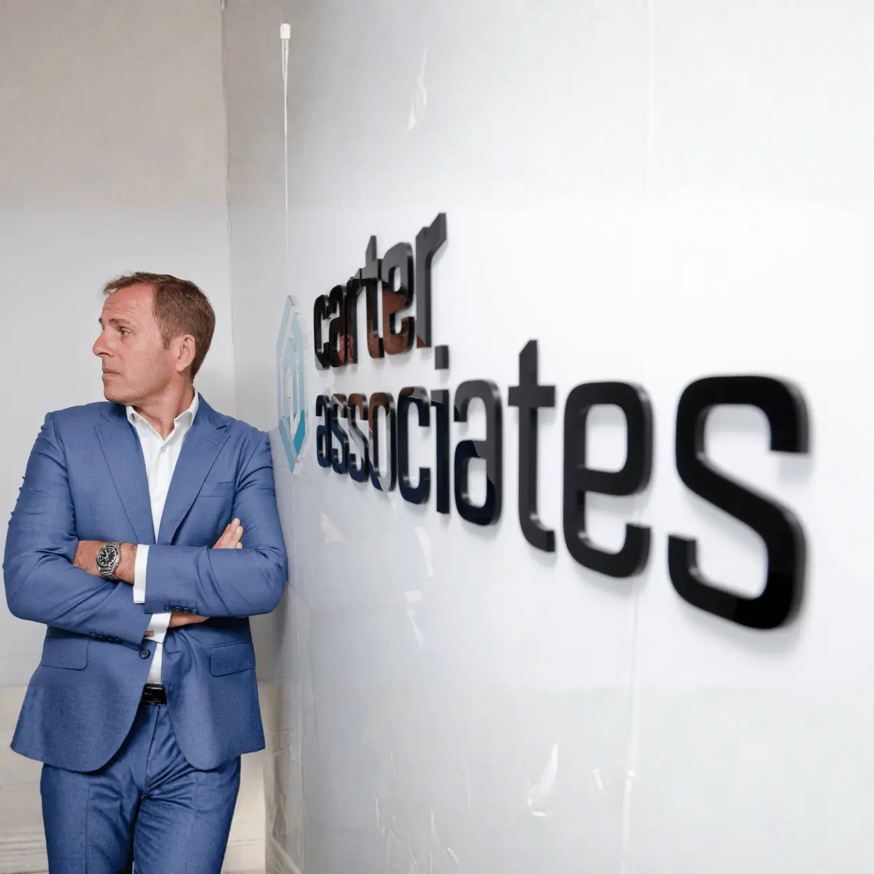 Professional man in blue suit stands confidently beside "Carter Associates" wall sign