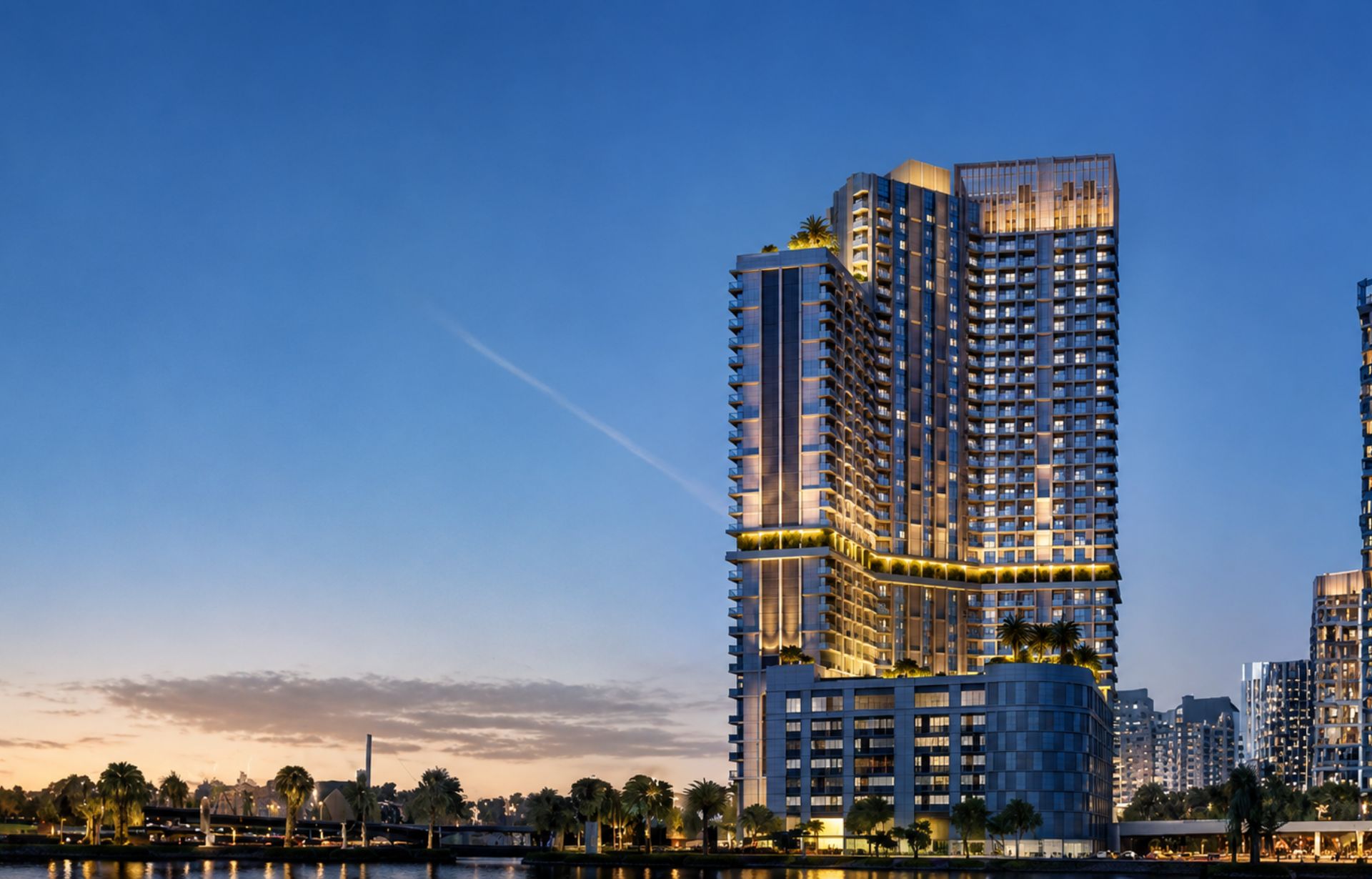 Modern illuminated high-rise residential towers at dusk reflecting in waterfront with palm trees.