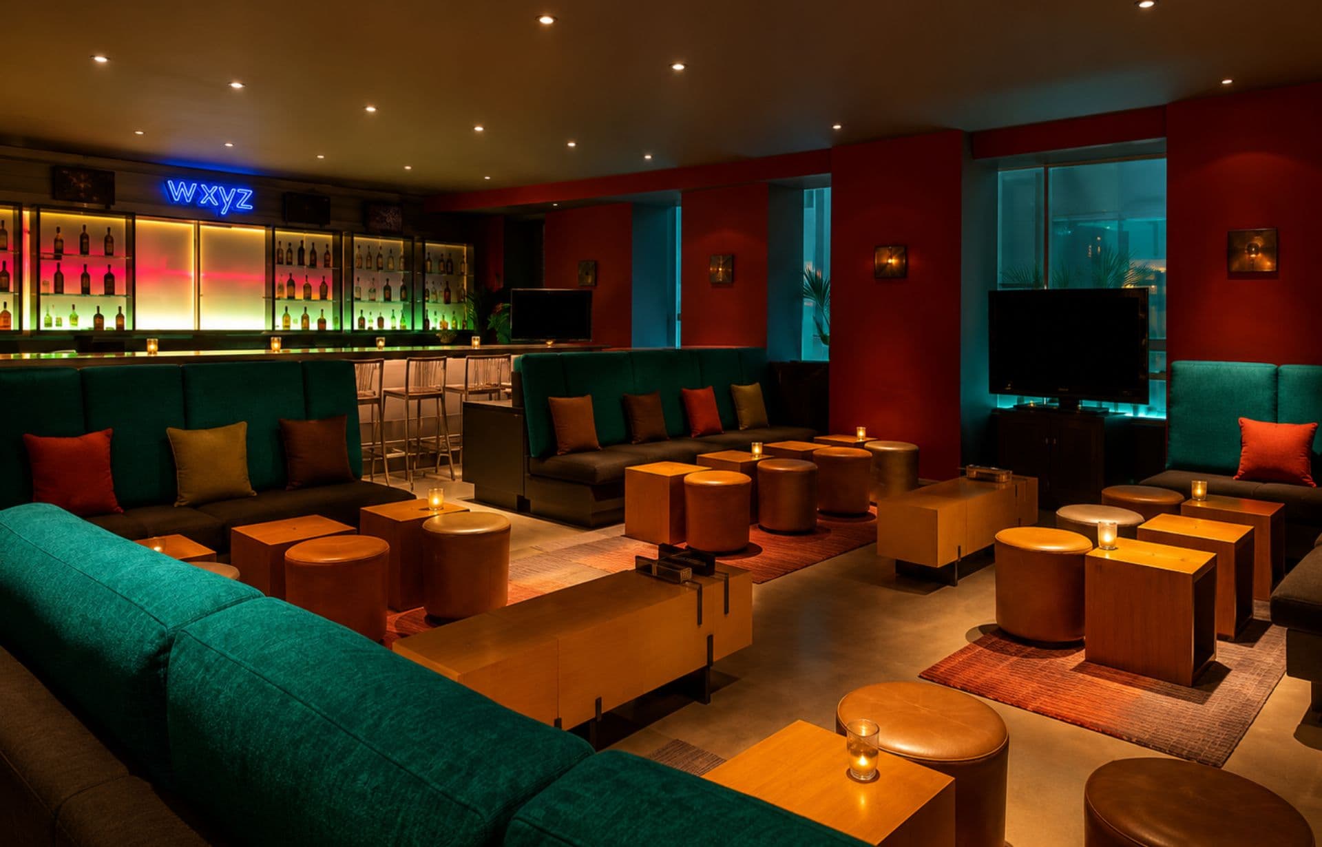Modern nightclub lounge with turquoise seating, orange tables, and illuminated bar with "WXYZ" neon sign