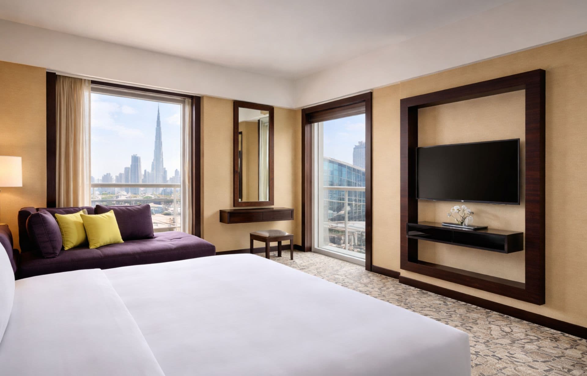 Luxury hotel bedroom with white bed, purple sofa, and cityscape view through floor-to-ceiling windows.