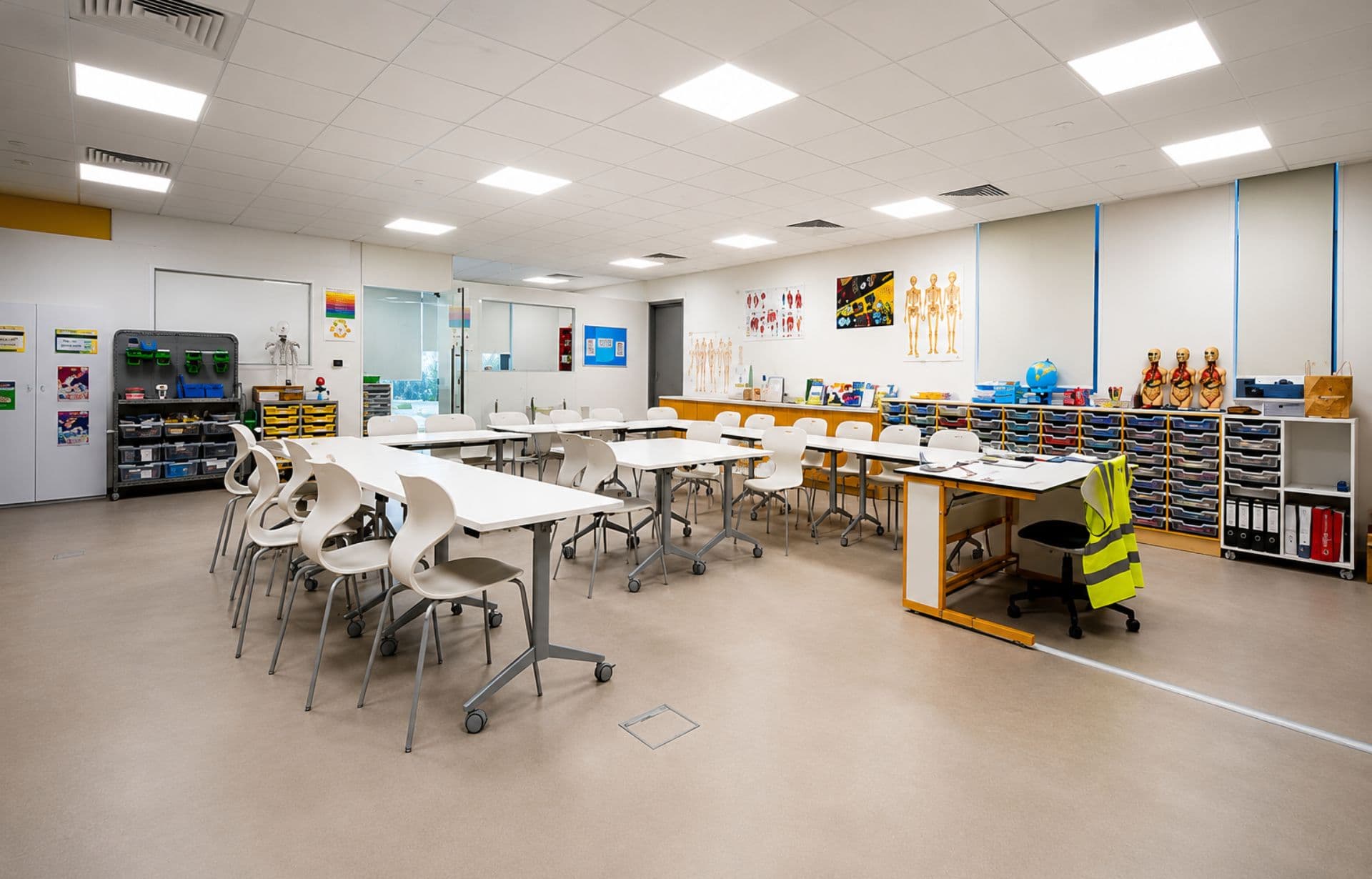 Modern school classroom with white chairs, collaborative workstations, storage bins, and educational wall displays.