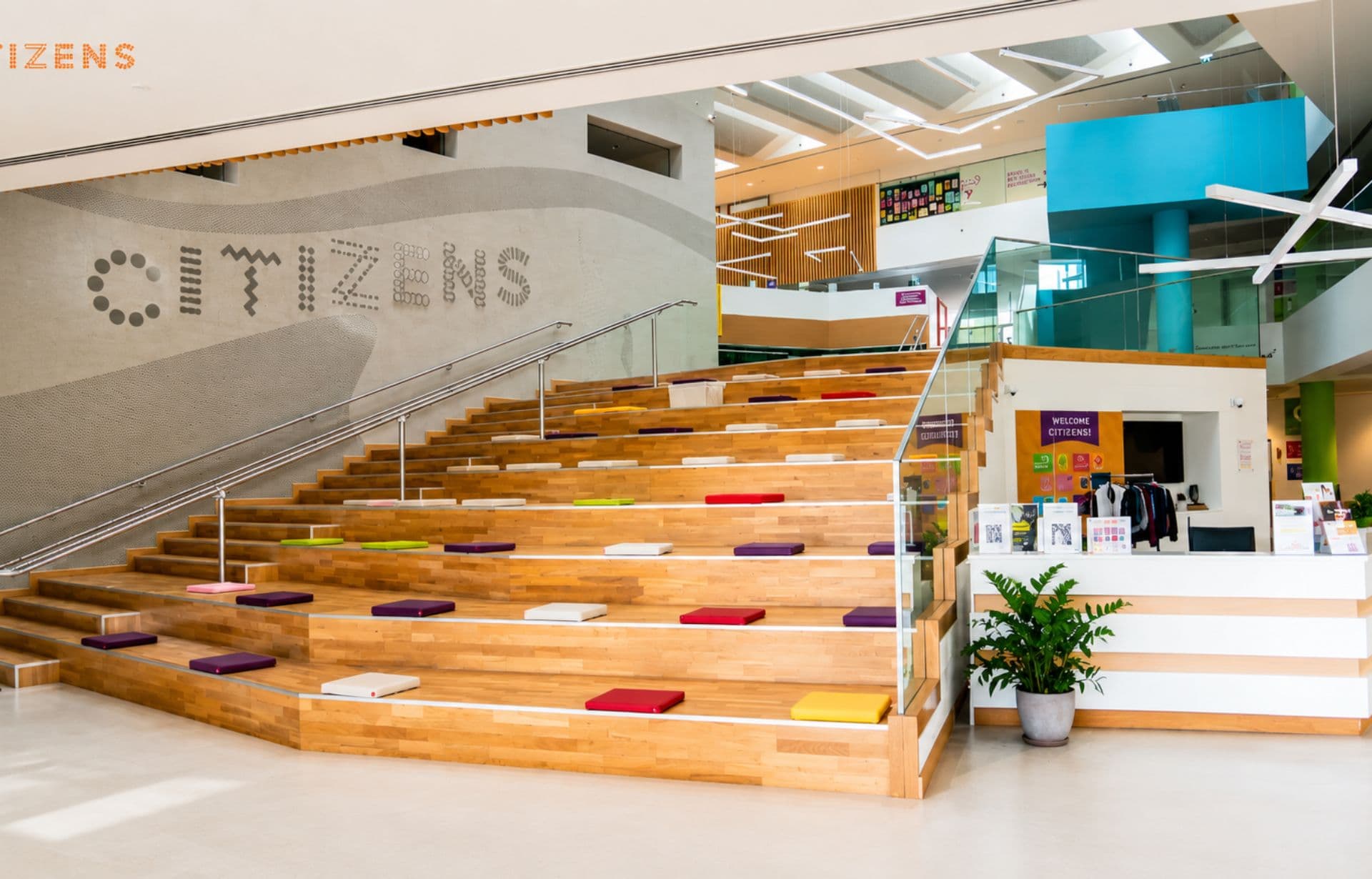 Modern Citizens museum interior with wooden steps, colorful cushions, and blue architectural elements.