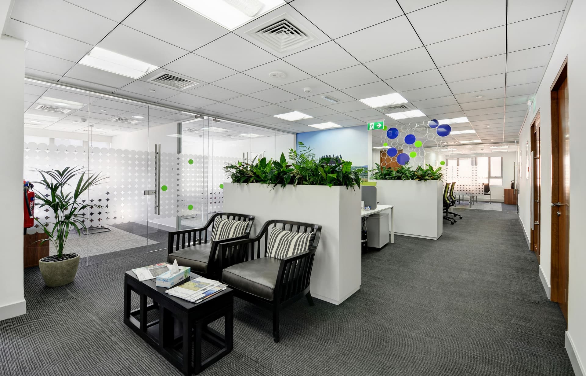 Modern office lobby with black furniture, plants, glass partitions, and hanging decorative spheres