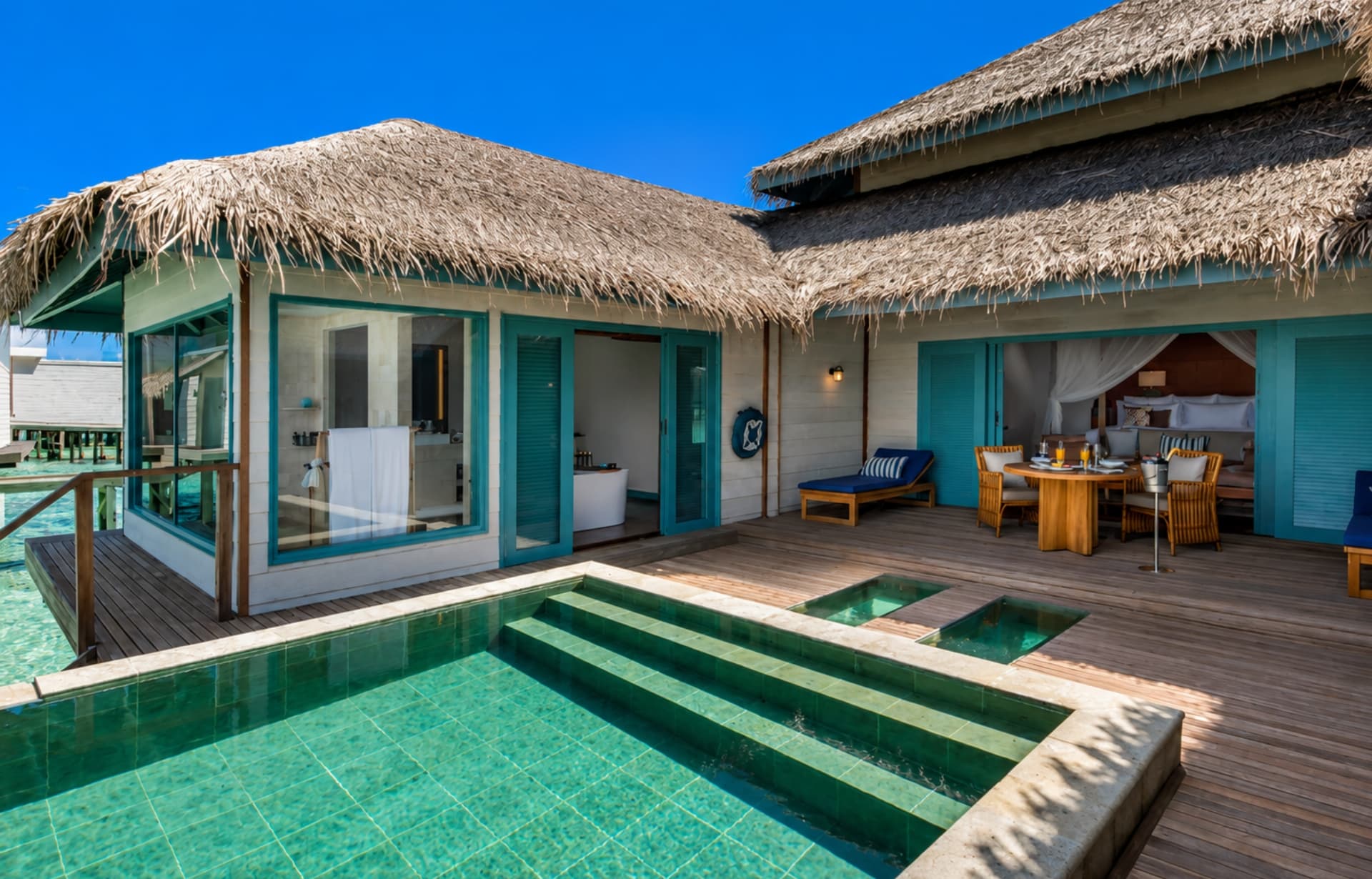 Tropical overwater bungalows with thatched roofs, turquoise pool, and clear blue sky