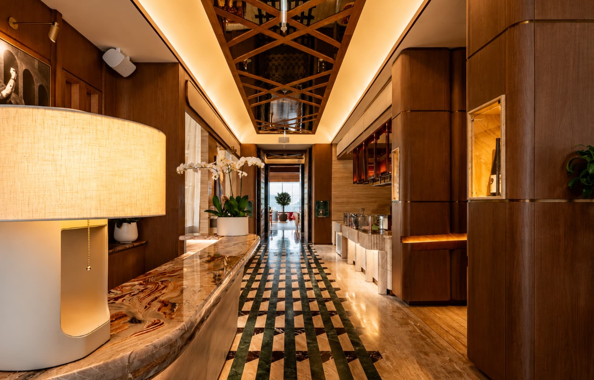 Luxury hotel corridor with marble flooring, wood paneling, and warm ambient lighting throughout