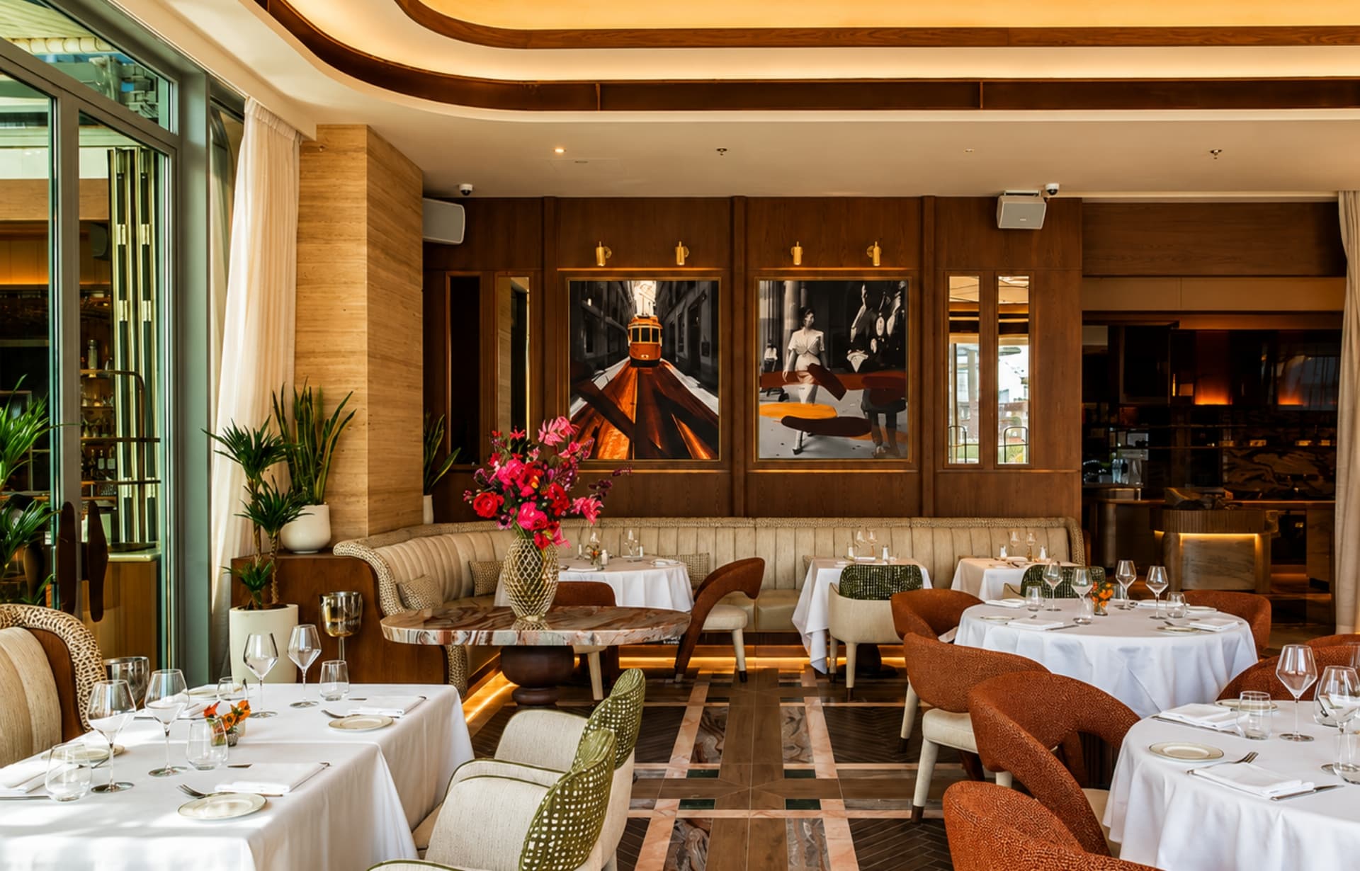 Upscale restaurant dining room with wood paneling, round white-tablecloth tables, and modern artwork.