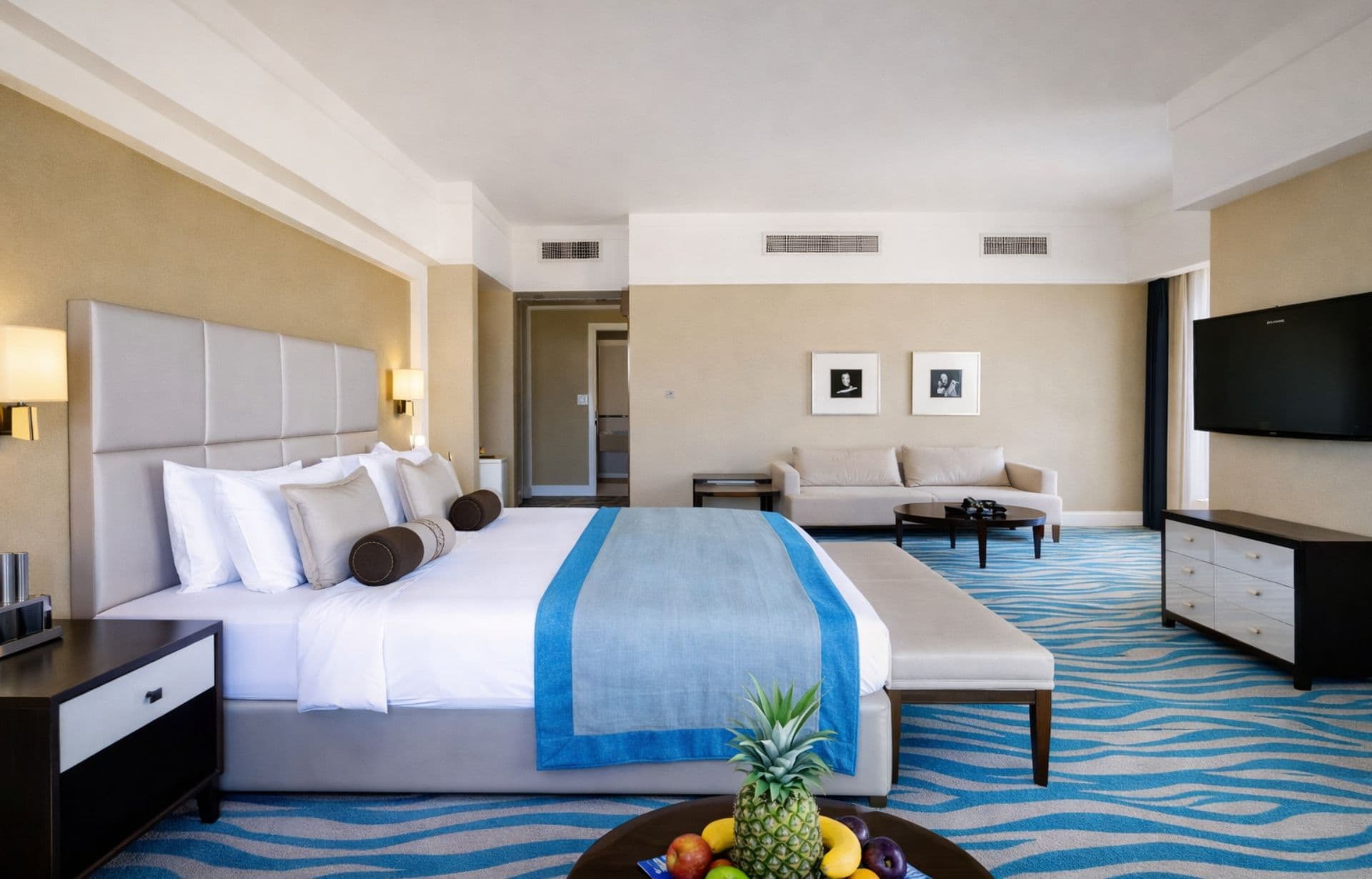 Spacious luxury hotel room with king bed, blue accent stripe, sofa, and modern furnishings.