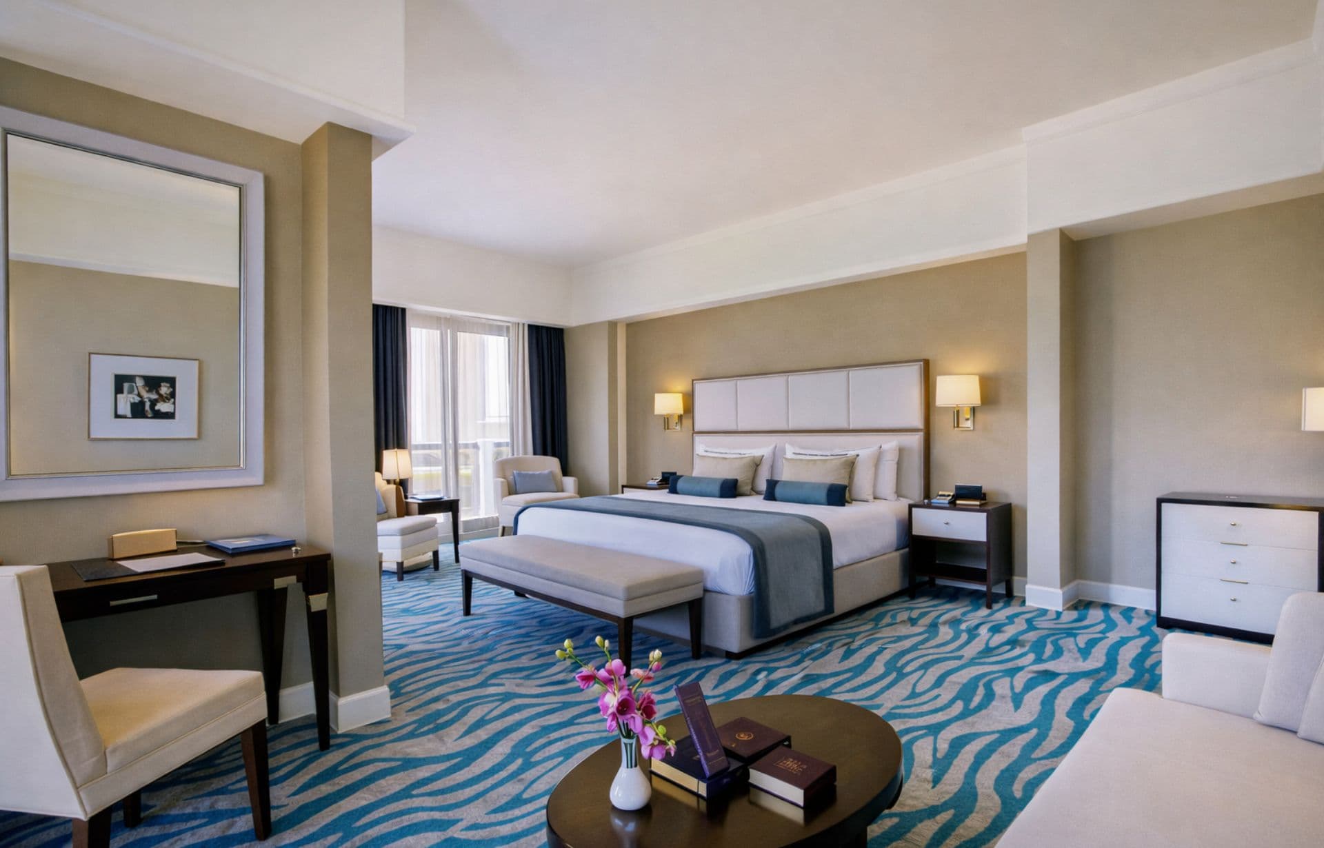 Luxury hotel suite with king bed, elegant furnishings, and blue striped carpet.
