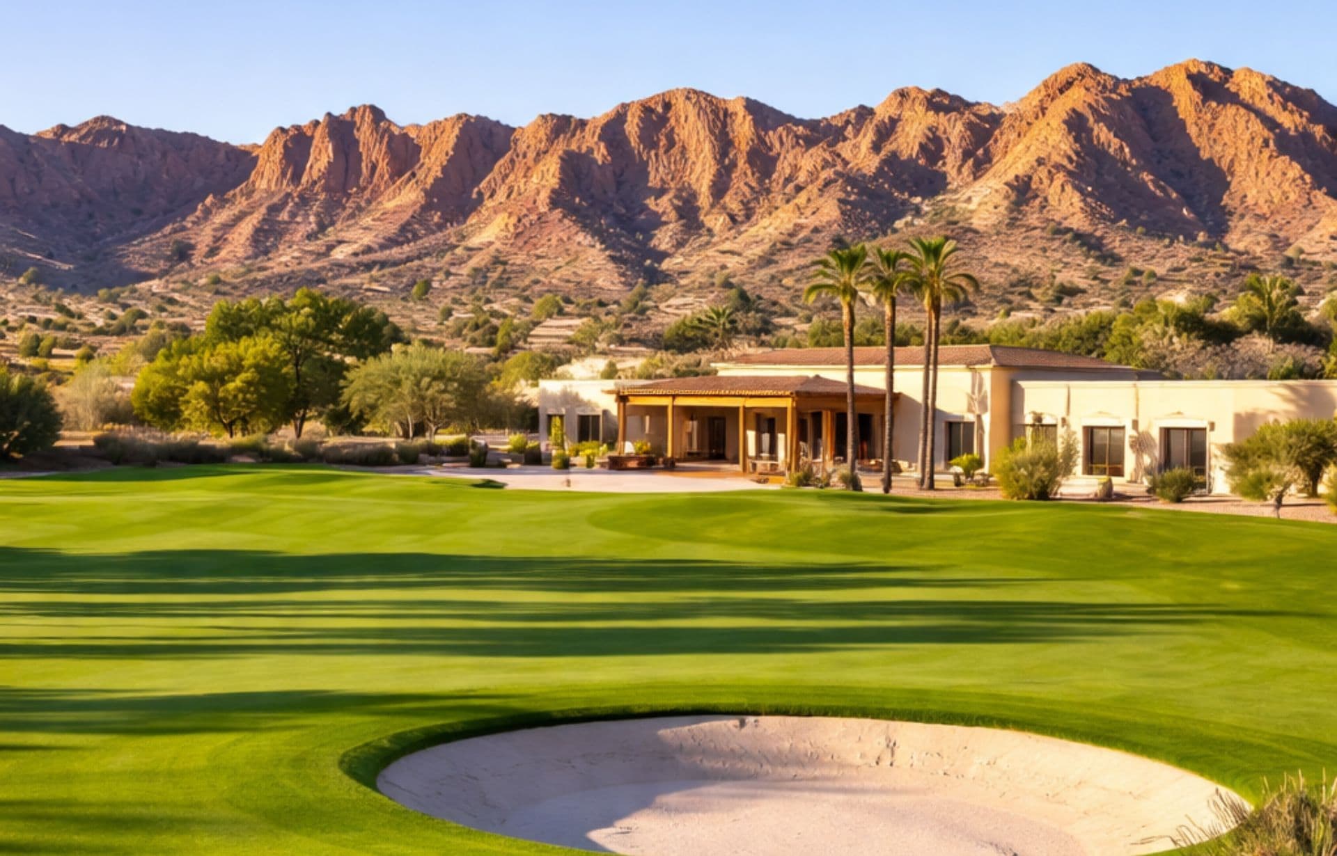 Luxury resort with golf course, sandy bunker, and palm trees overlooking desert mountains.