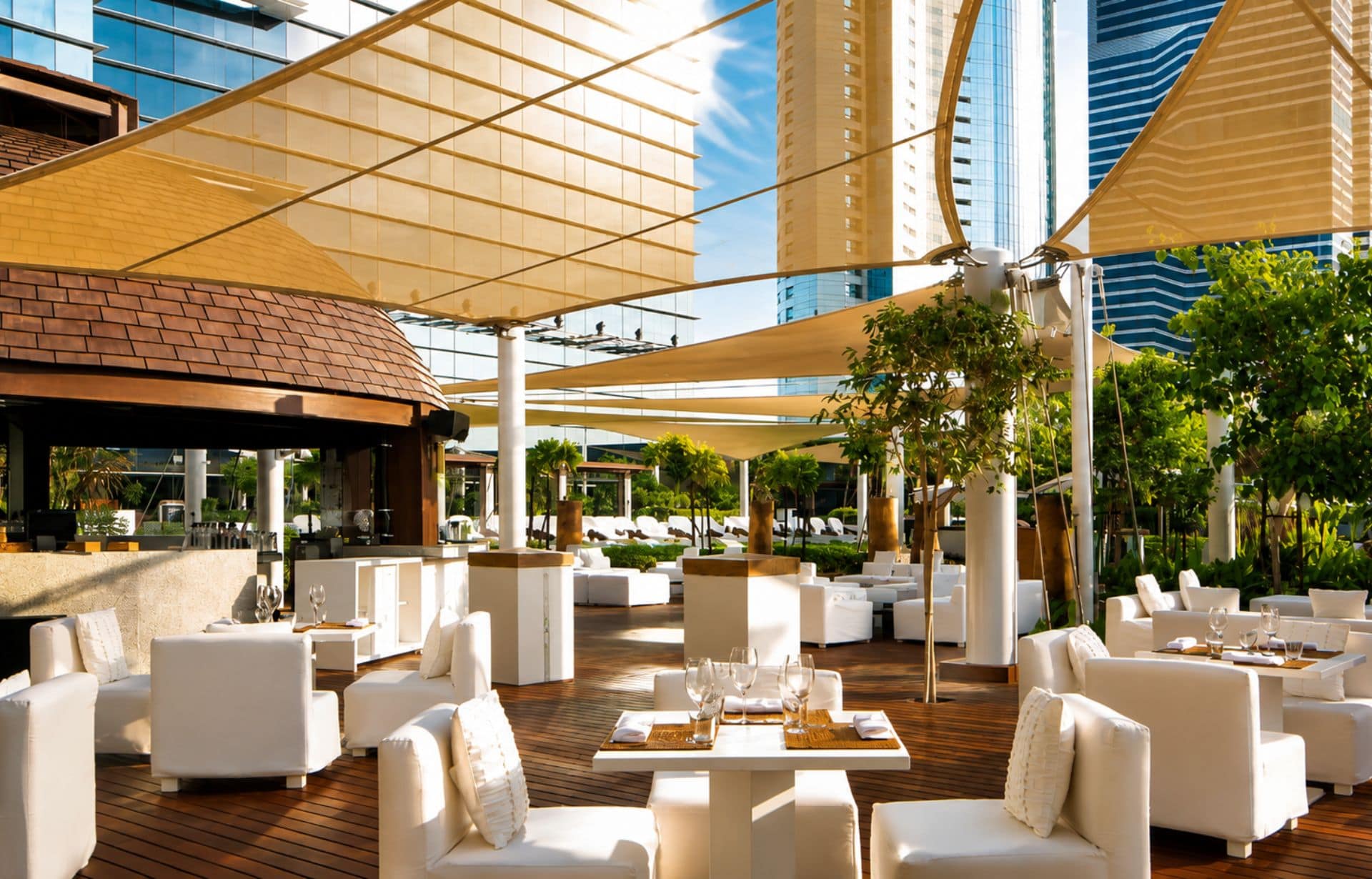 Modern rooftop restaurant patio with white furniture, golden shade sails, and city skyline views