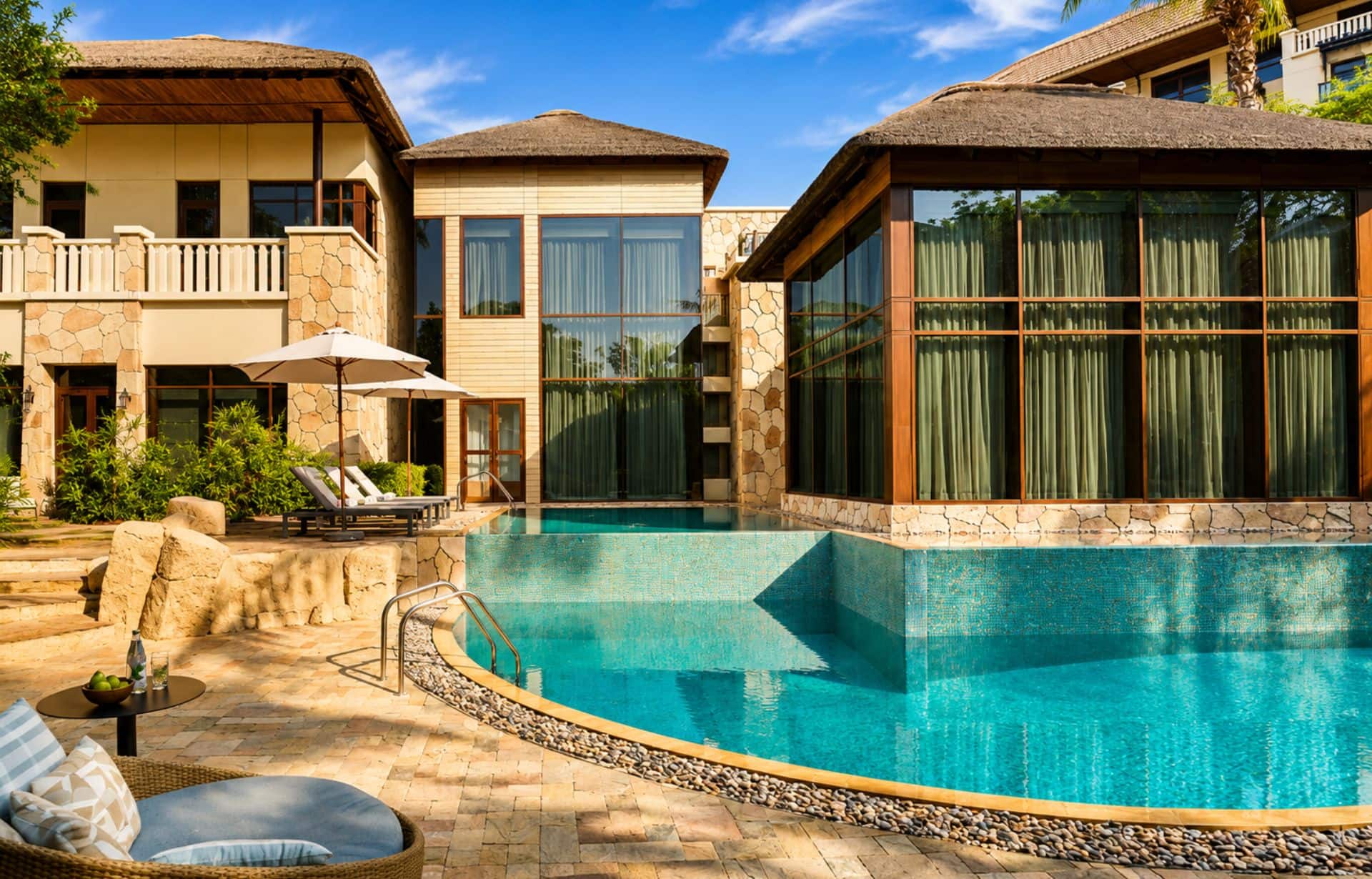 Luxury resort courtyard with turquoise pool, thatched-roof buildings, and stone architecture