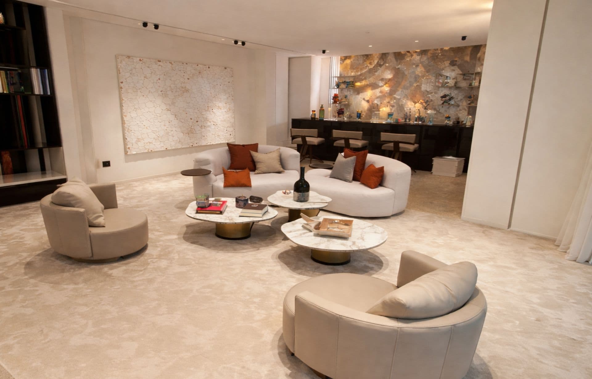 Modern luxury living room with cream furniture, marble tables, and textured stone accent wall.