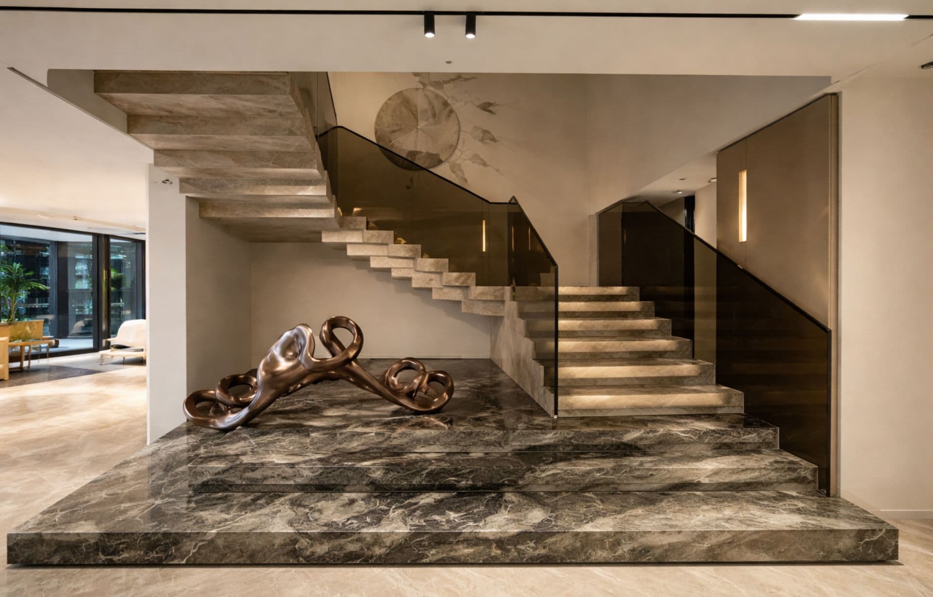Modern luxury home interior with marble platform, wooden stairs, glass railings, and bronze sculpture