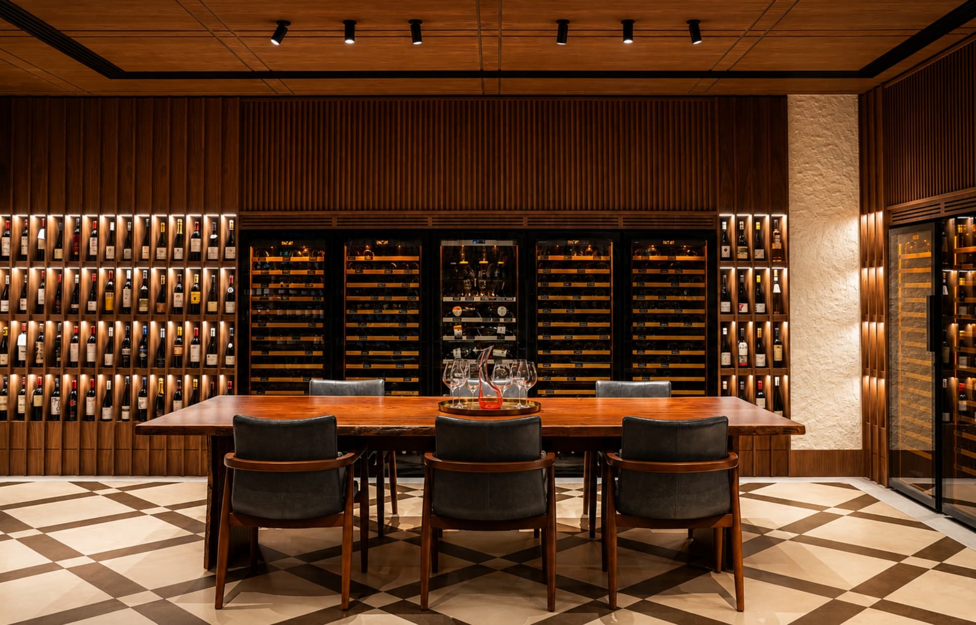 Modern wine cellar with extensive bottle storage, wooden table, black chairs, and temperature-controlled display cabinets.