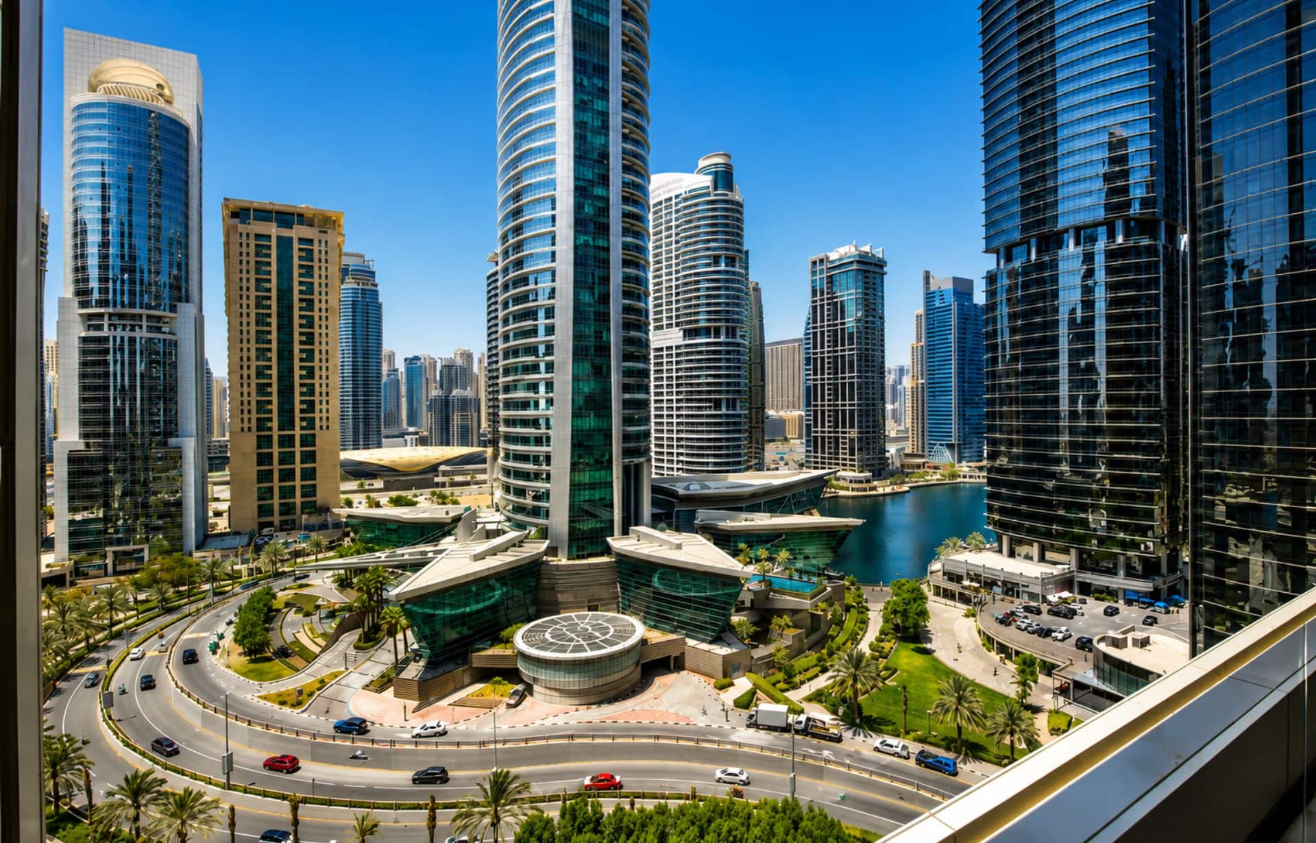 Modern waterfront city skyline with residential towers, marina, and palm trees under clear blue sky