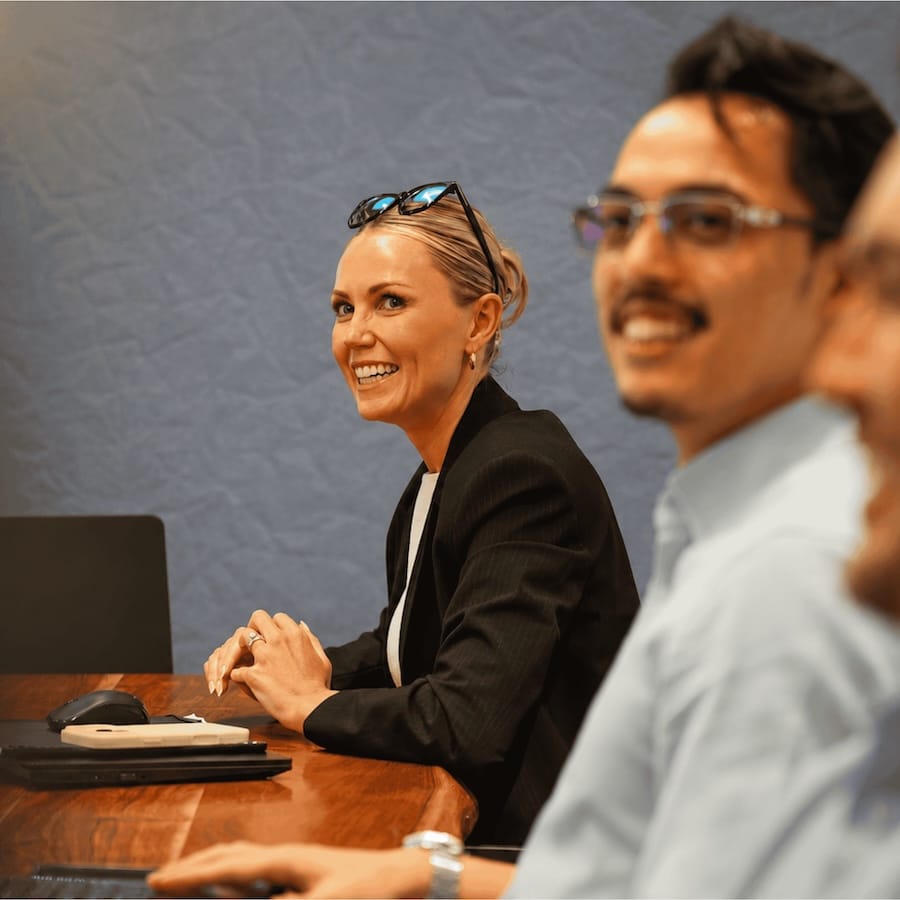Smiling woman in black blazer sits at table during business meeting with colleagues