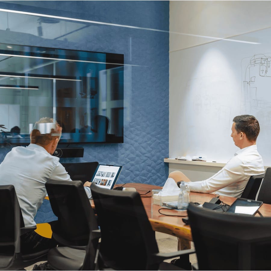 Two men in modern office with glass partition, laptop, and whiteboard sketch visible