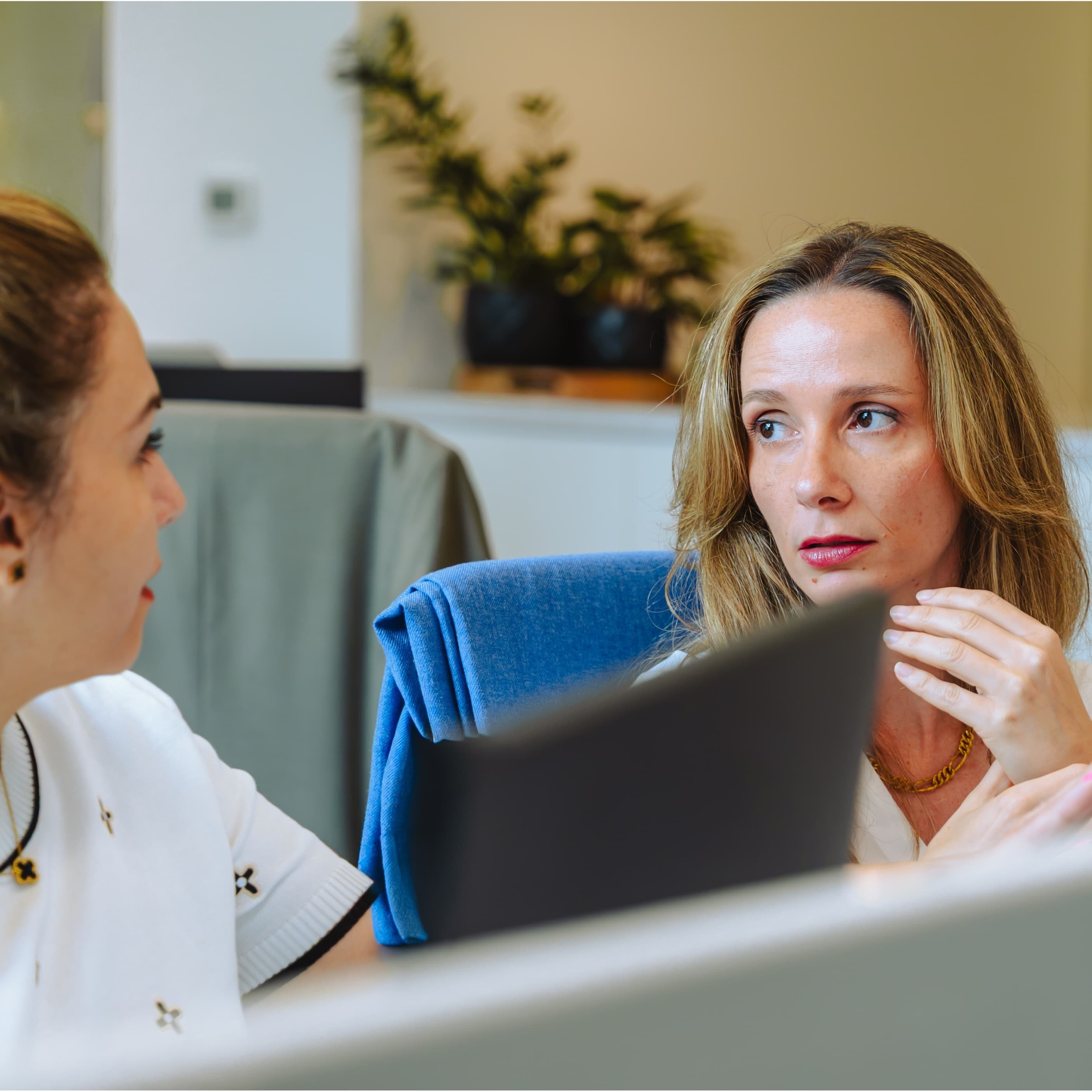 Two women discussing content on a tablet in a modern office setting with plants.
