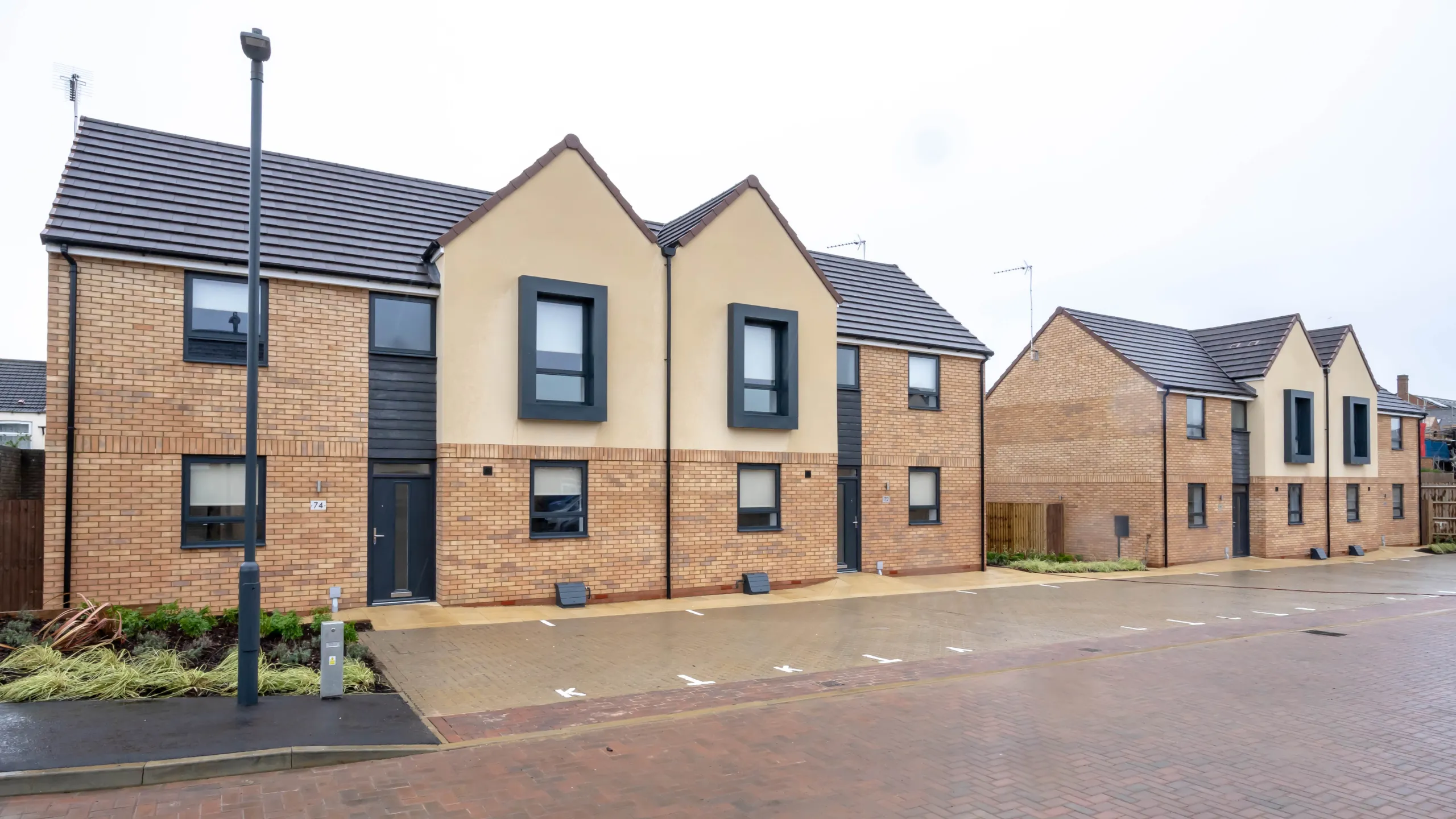 Row of modern two-story townhouses with brick and cream stucco facades and designated parking spaces in front.