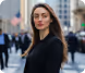 Confident woman in black blazer standing on a city street with blurred pedestrians in background.