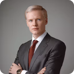 Professional young man with blonde hair in a dark suit and red tie against a plain background.