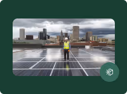 Worker wearing safety gear inspecting solar panels on a rooftop with a city skyline and cloudy sky in the background.