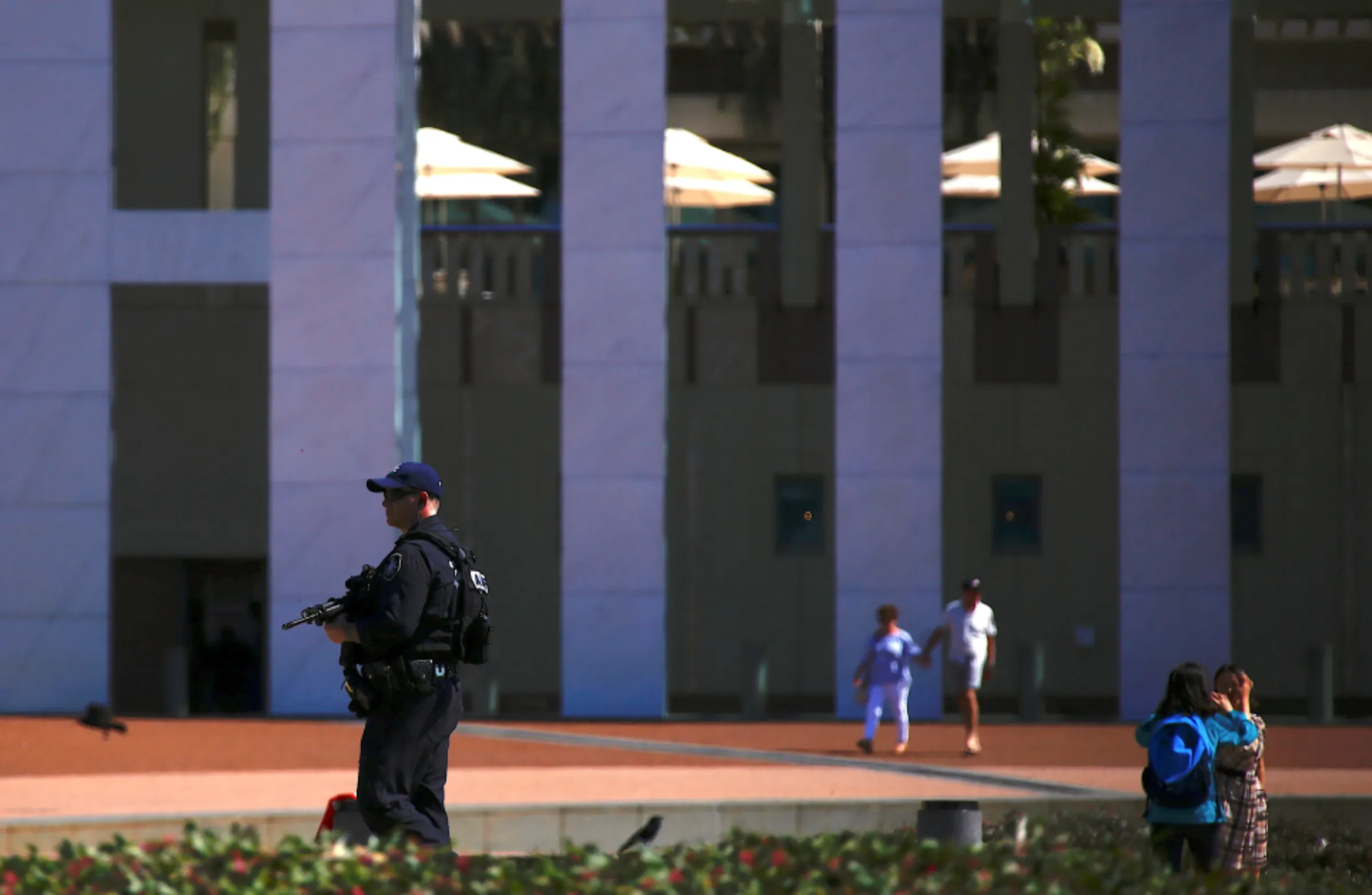 Toeristen maken foto's en lopen in de buurt van een Australische federale politieagent met een pistool terwijl hij patrouilleert op het voorplein van het Australische parlementsgebouw in Canberra, Australië, 16 oktober 2017