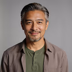 Middle-aged man with salt-and-pepper hair smiling, wearing a brown jacket over a green shirt.