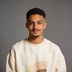Young man with curly hair and mustache wearing a white sweatshirt against a gray background.