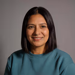 Smiling woman with straight black hair wearing a teal sweatshirt against a gray background.