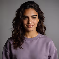 Woman with long curly hair wearing a purple sweatshirt smiling against a gray background.