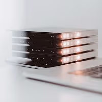 Stack of closed black laptops with glowing keyboard lights placed on a white surface.