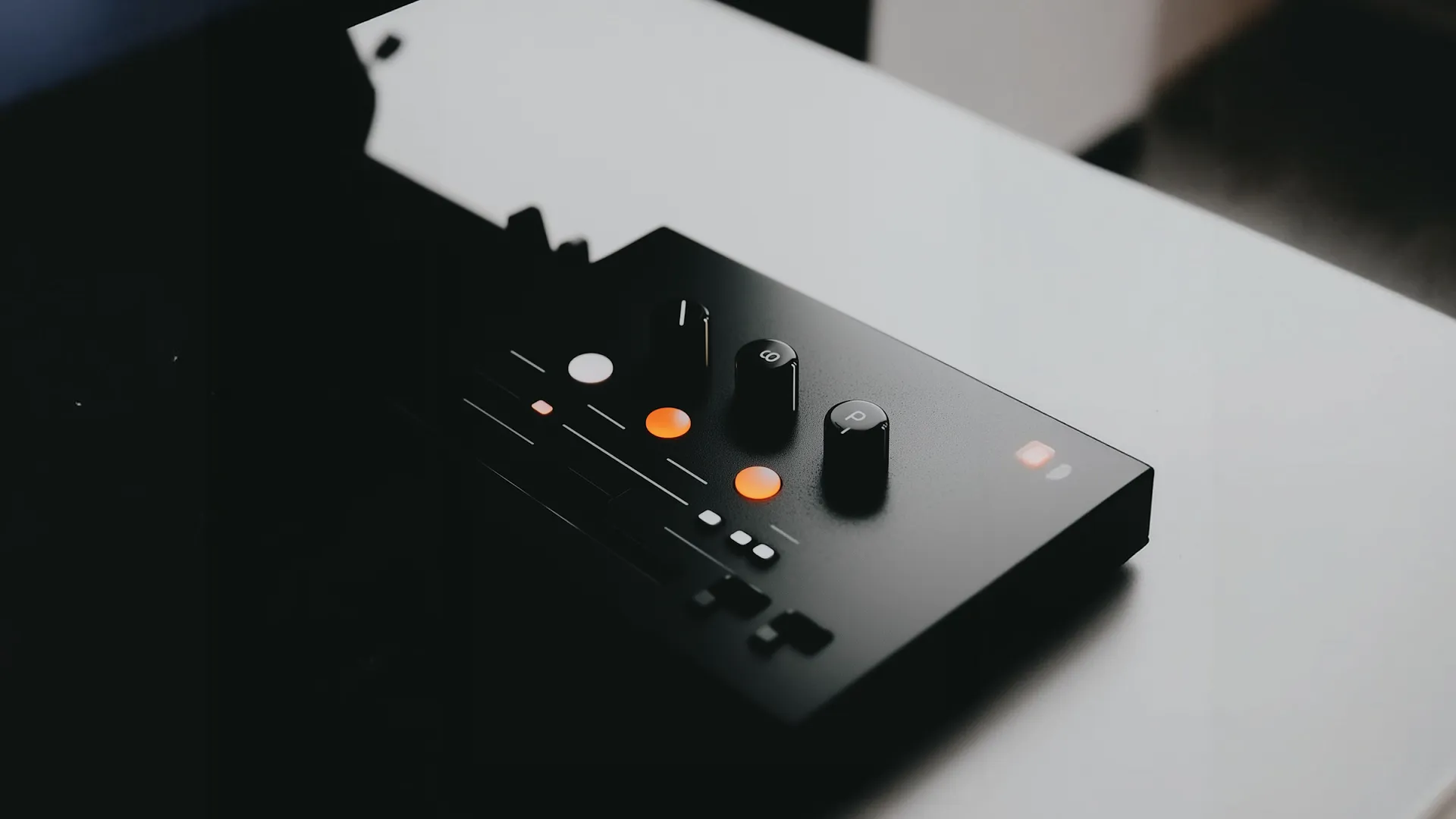 Close-up of a black audio controller with knobs and illuminated buttons on a white surface.