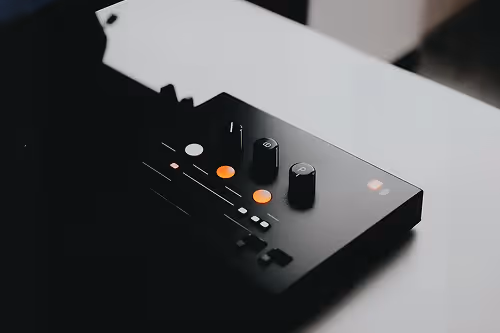 Close-up of a black electronic device with knobs and illuminated buttons on a white surface.
