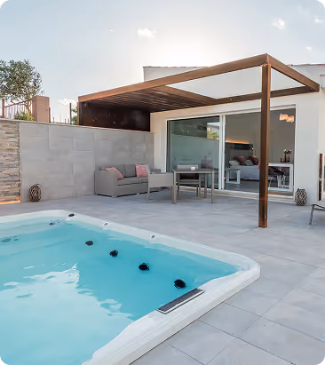 Terrasse moderne avec piscine rectangulaire, canapé, table avec chaises sous une pergola en bois, façade vitrée d'une maison.