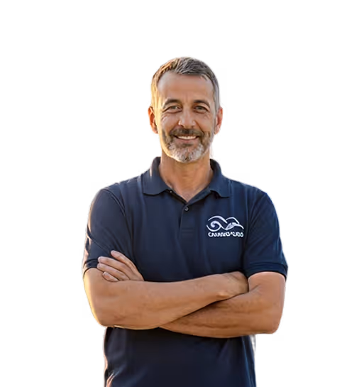 Homme souriant aux cheveux gris, bras croisés, portant un polo bleu marine avec un logo blanc.