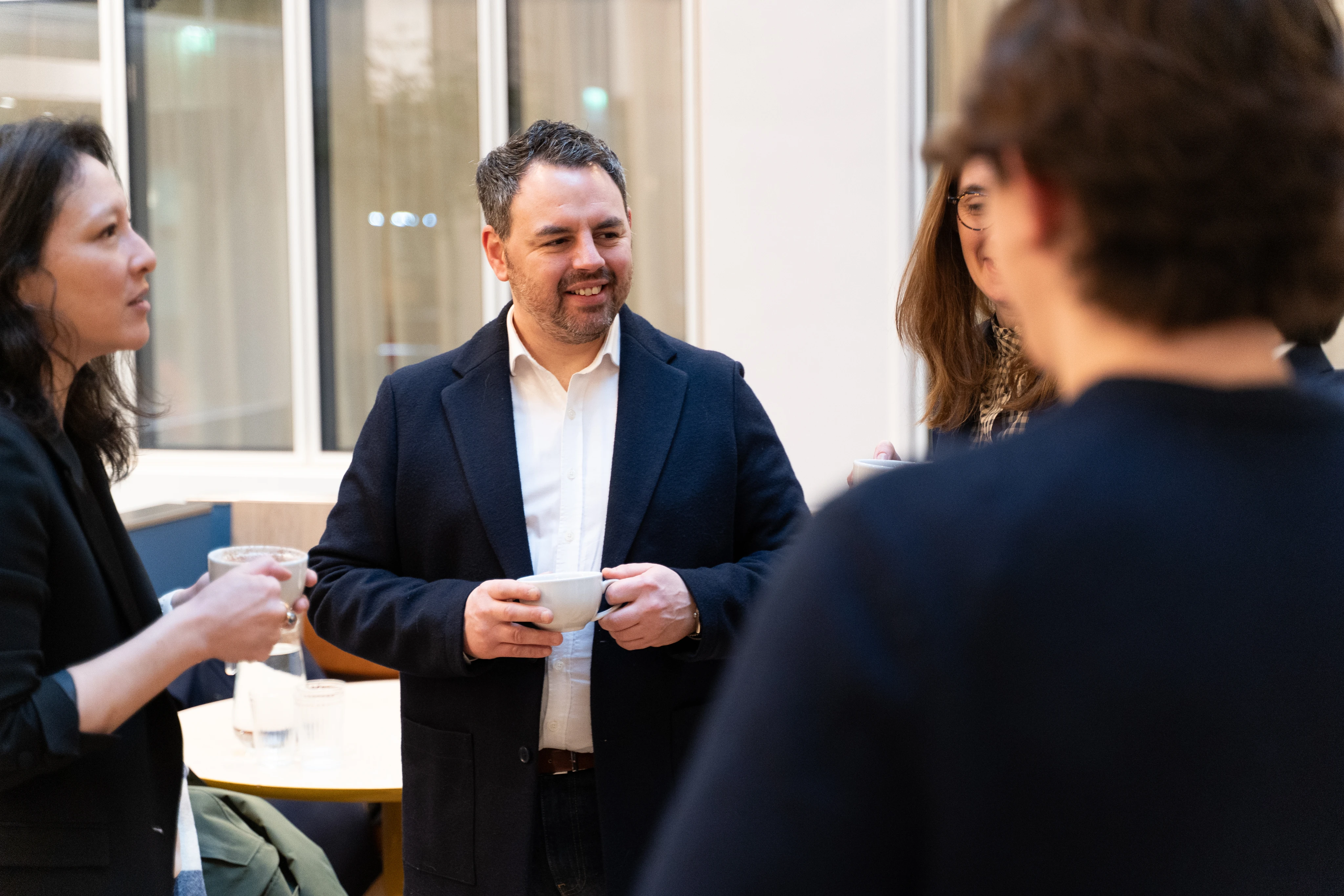Un groupe de quatre personnes discutant en tenant des tasses de café dans un espace intérieur lumineux.