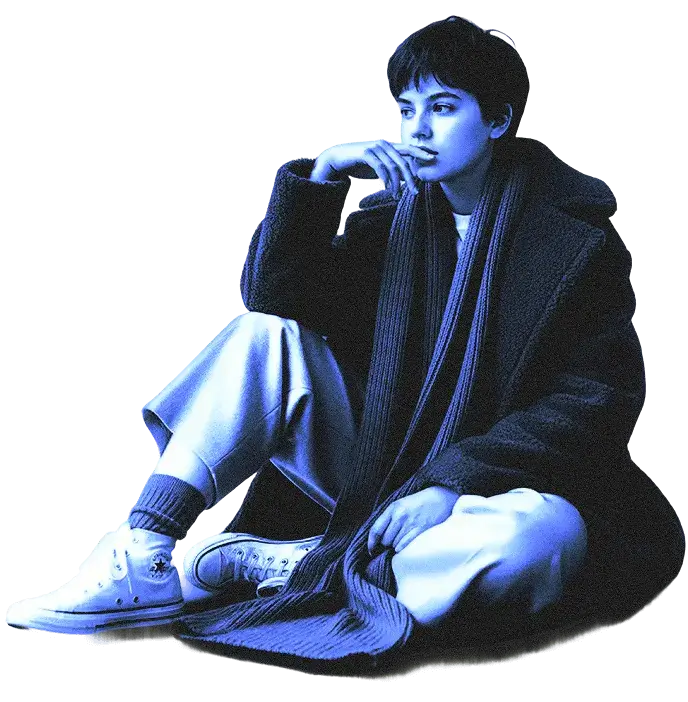 Людина сидить, схрестивши ноги, у светрі та довгому шарфі, у білих кросівках на темному тлі, підсвіченому синіми тонами.