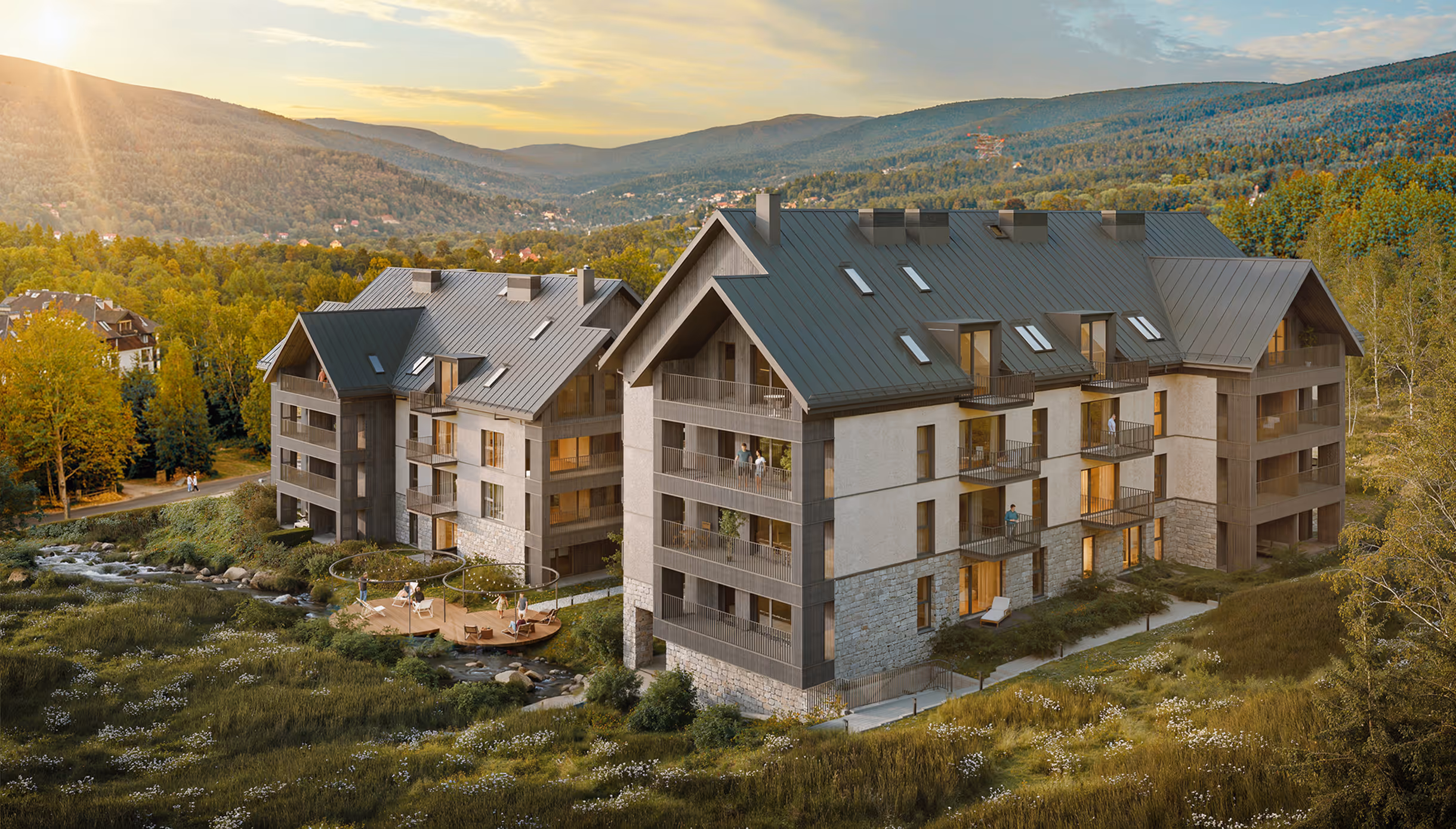 Modern apartment buildings with balconies near a small river, surrounded by green fields and forested hills at sunset.