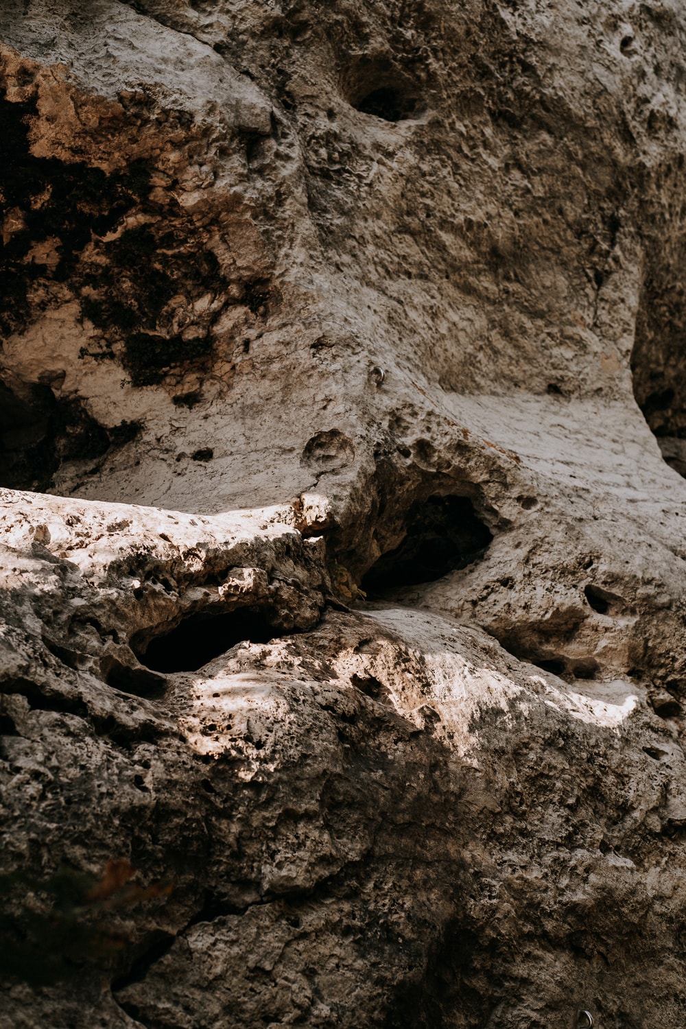 Close-up of a textured, weathered rock formation with shadows highlighting its uneven surface and small holes.