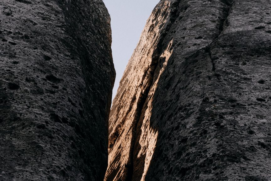 Narrow gap between tall textured rock formations with sunlight casting shadows on one side.
