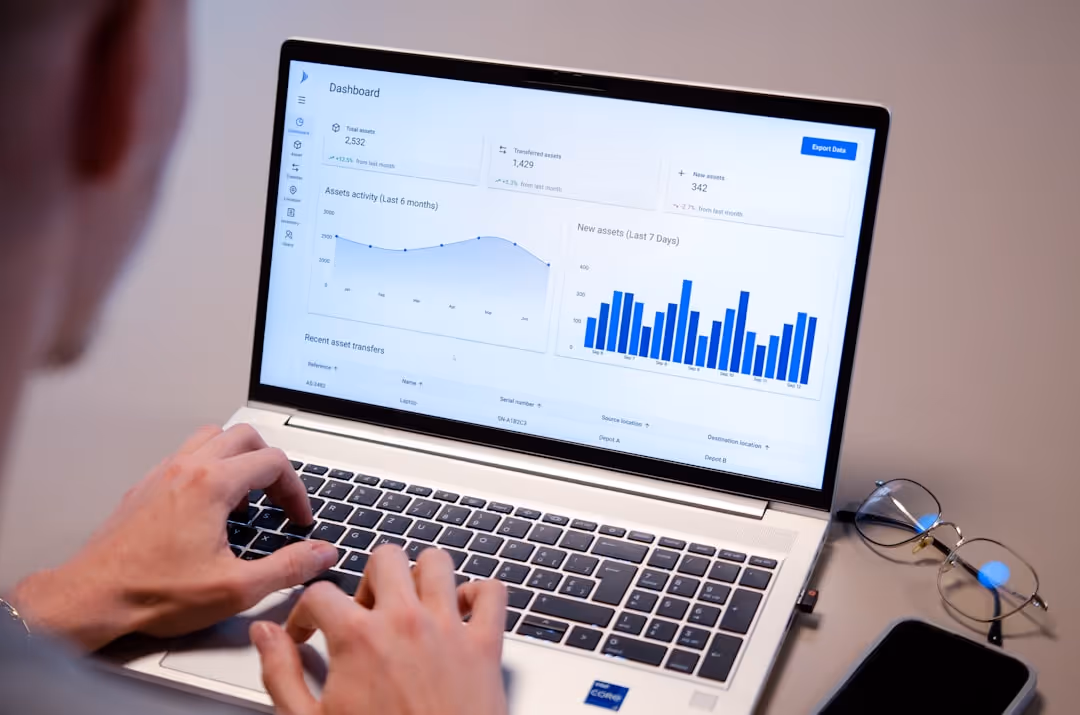 Person typing on a laptop showing a dashboard with asset data and charts.