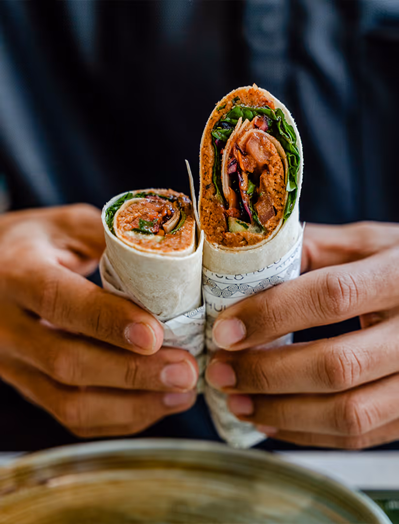 Zwei Hälften eines mit Gemüse, Salat und einer veganen Füllung gefüllten Wraps, von einer Person gehalten.